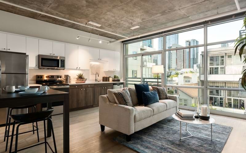 a spacious renovated living room with a couch and kitchen and floor to ceiling windows